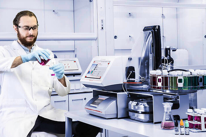 A lab technician prepares a sample next to an Anton Paar DMA 4500 M density meter with Xsample 530 sample changer and label printer.