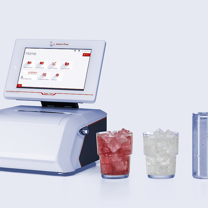 Anton Paar Lyza 7000 FTIR spectrometer beside two ice-filled glasses with red and clear liquids and a silver beverage can.