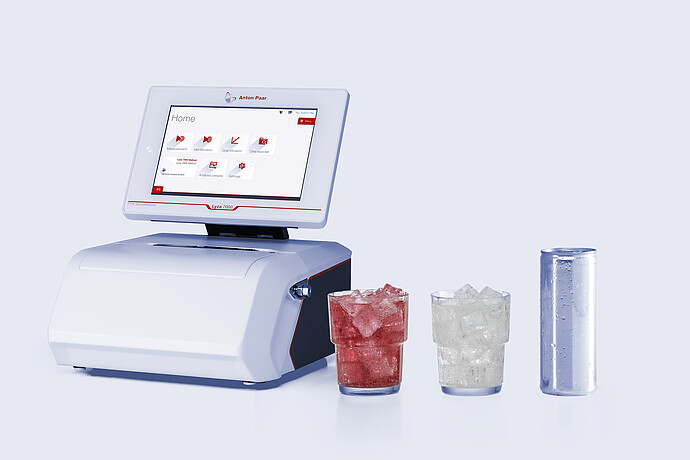 Anton Paar Lyza 7000 FTIR spectrometer beside two ice-filled glasses with red and clear liquids and a silver beverage can.