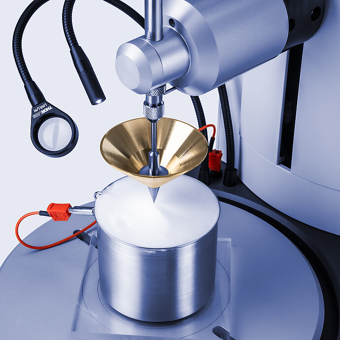 Close-up of Anton Paar Penetrometer PNR 500 with brass cone penetrating white semisolid sample in metal cup, with temperature sensor attached.