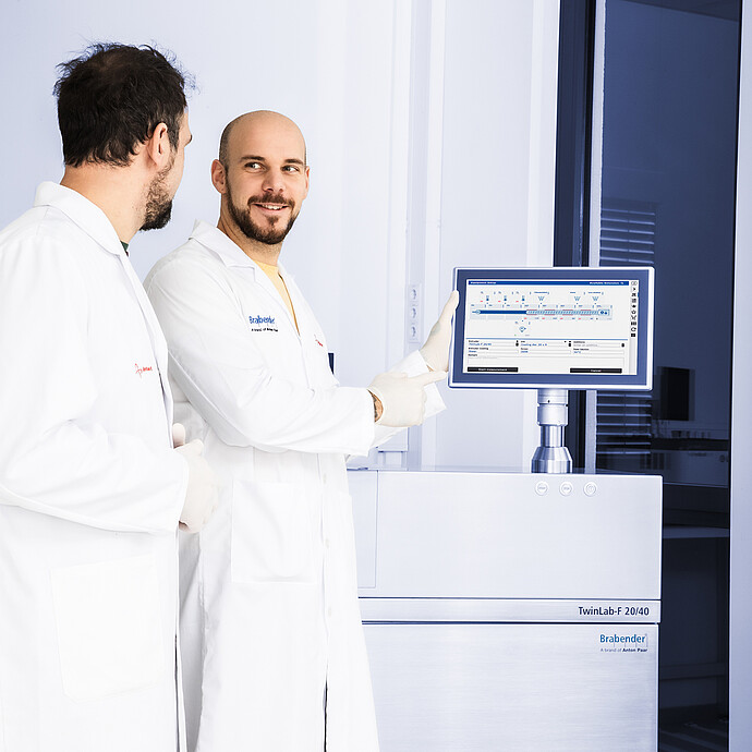 Two lab workers at Brabender TwinLab-F 20/40 TwinLab Series extruder, pointing to the touchscreen setup screen.