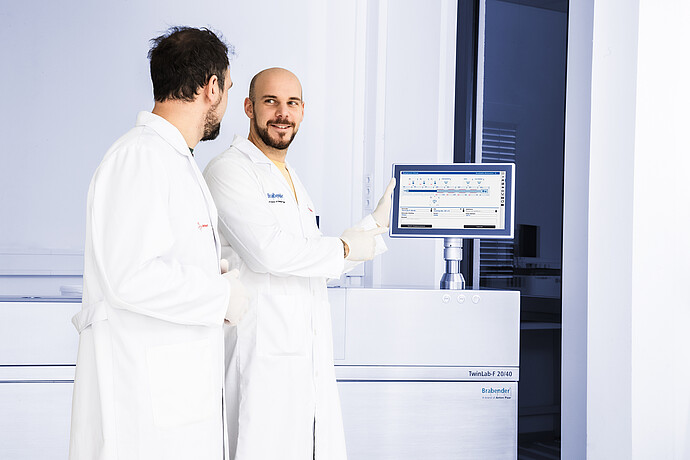 Two lab workers at Brabender TwinLab-F 20/40 TwinLab Series extruder, pointing to the touchscreen setup screen.