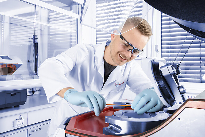 Lab technician in safety gear working with a precision instrument under a protective hood in a clean, modern laboratory setting.