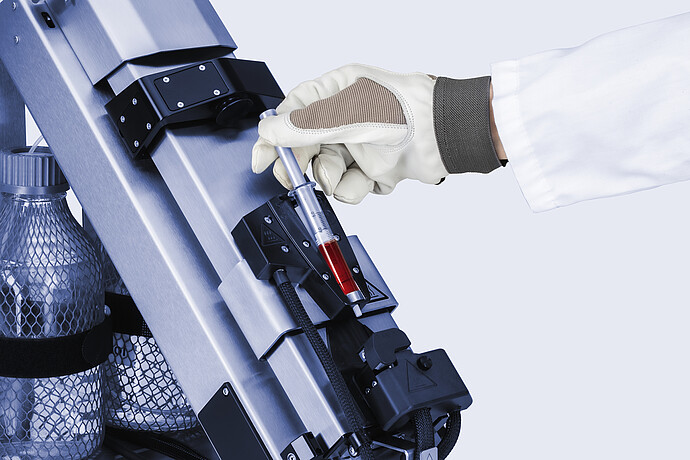Gloved technician loading red sample into a heated syringe holder on the Anton Paar Xsample 610 sample changer