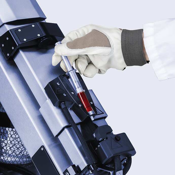 Gloved technician loading red sample into a heated syringe holder on the Anton Paar Xsample 610 sample changer