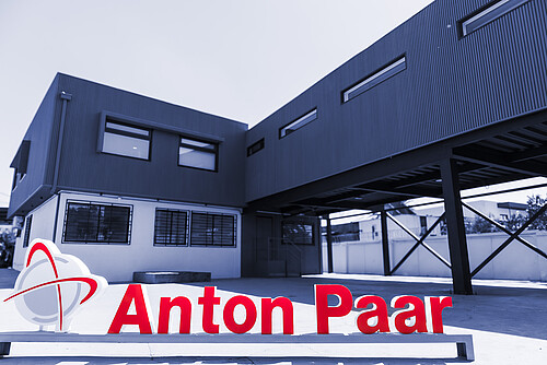 Anton Paar Chile building with dark metal facade and elevated structure, red Anton Paar logo sign in foreground courtyard