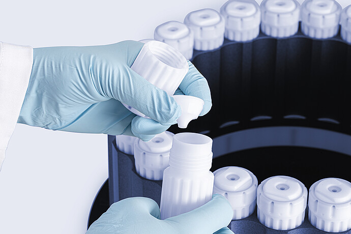 Gloved hands assembling HVT Rotor vessel, placing sealing insert into open digestion vessel, with rotor and capped vessels in the background