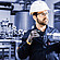 Coriolis flow meter L-Cor 8000 held by a technician in protective gear, standing in an industrial piping system with valves and gauges.