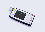 Anton Paar Cora 101 handheld Raman spectrometer lying on a flat surface with its display showing scan menu options.