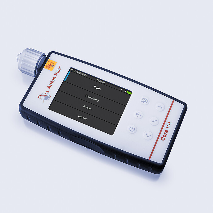 Anton Paar Cora 101 handheld Raman spectrometer lying on a flat surface with its display showing scan menu options.