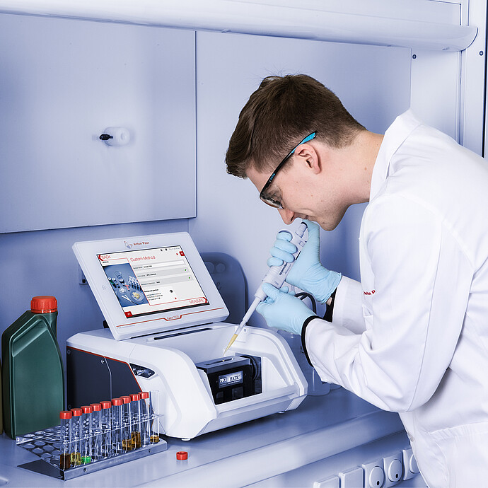Laboratory technician pipettes a liquid sample onto the Anton Paar Lyza 7000 FTIR spectrometer while its touchscreen shows a custom method.