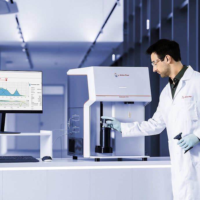Lab technician loading a sample into the Anton Paar Autosorb 3300, with measurement graphs shown on a monitor
