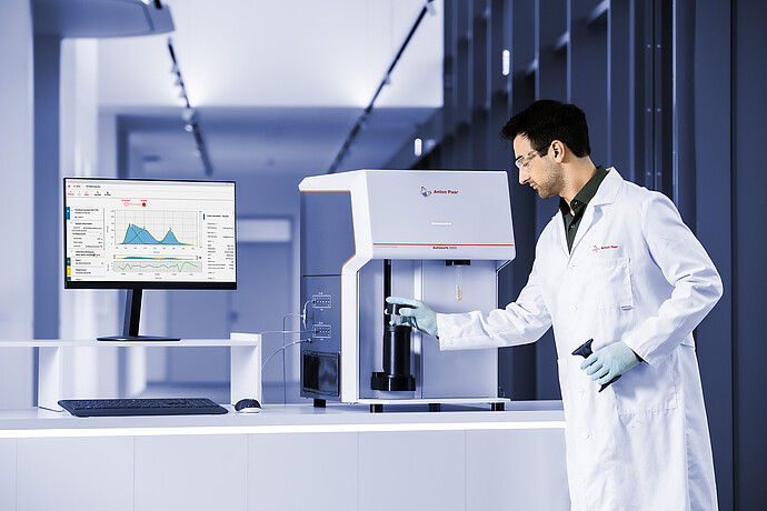 Lab technician loading a sample into the Anton Paar Autosorb 3300, with measurement graphs shown on a monitor