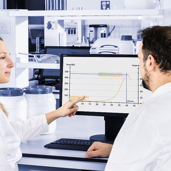 Two technicians reviewing viscosity curve on monitor, discussing measurement results from Brabender Amylograph-E in laboratory environment