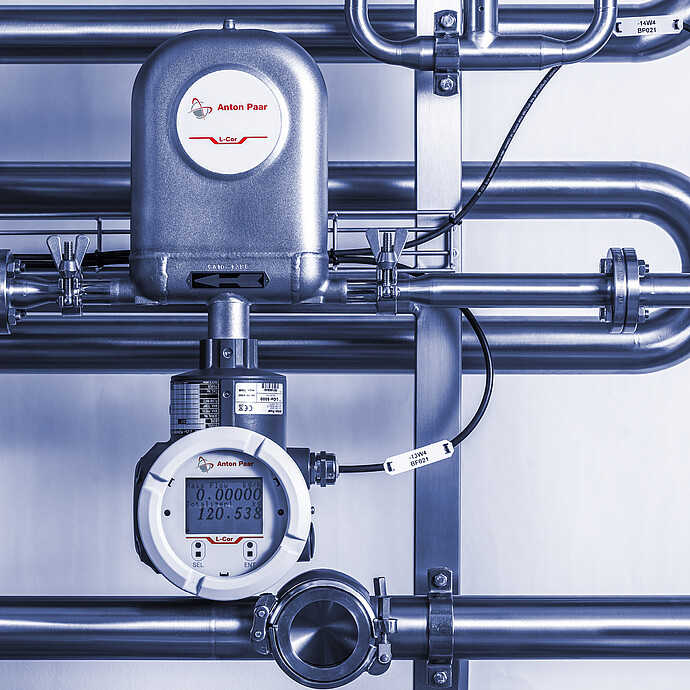 Installed Anton Paar L-Cor 8000 Coriolis flow meter with digital display mounted on stainless steel piping system with valves and sensor connections.