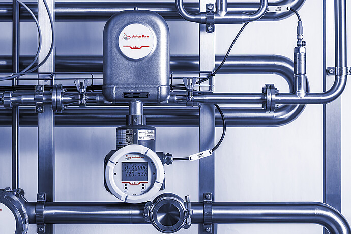 Installed Anton Paar L-Cor 8000 Coriolis flow meter with digital display mounted on stainless steel piping system with valves and sensor connections.