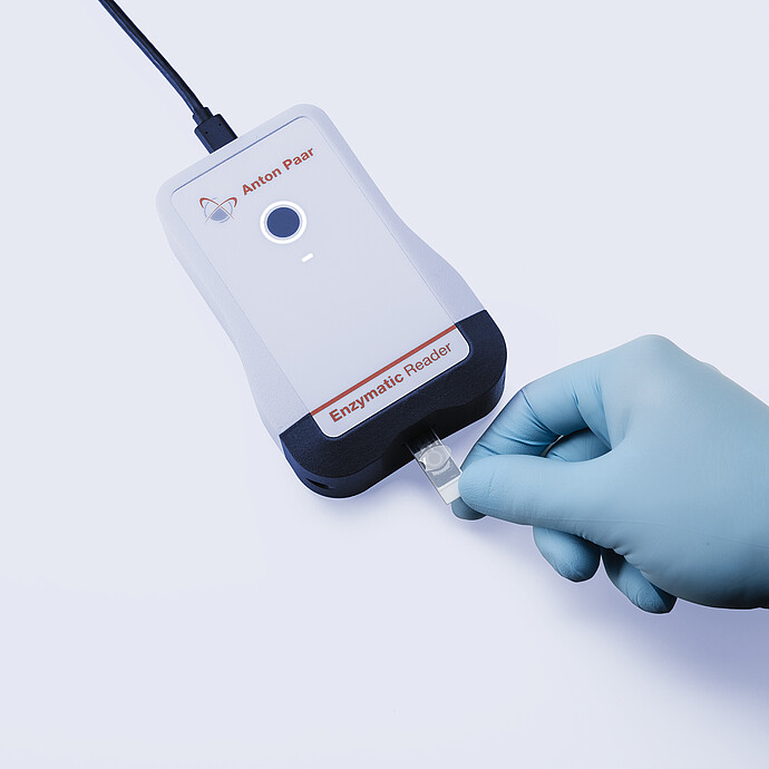 Anton Paar Enzymatic Reader digital ethanol meter with inserted test strip held by gloved hand on light gray background.