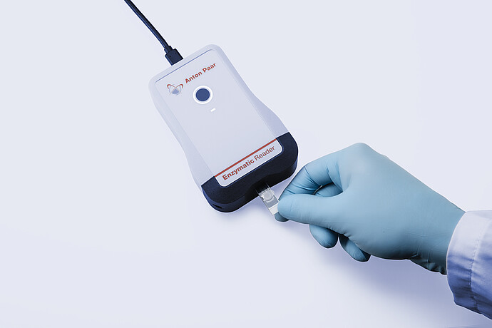 Anton Paar Enzymatic Reader digital ethanol meter with inserted test strip held by gloved hand on light gray background.