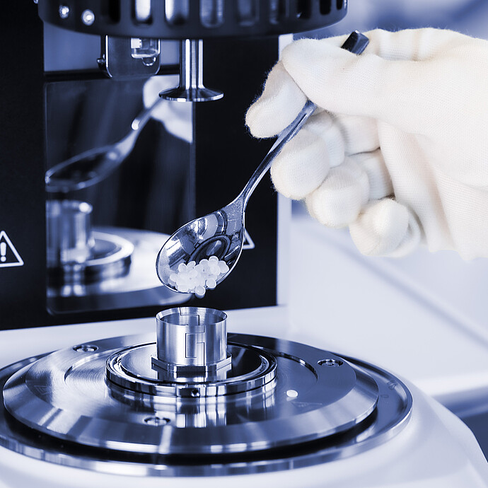 Gloved hand adds polymer pellets to the measuring cup of an Anton Paar SmartMelt polymer melt rheometer.