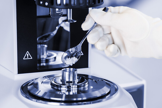 Gloved hand adds polymer pellets to the measuring cup of an Anton Paar SmartMelt polymer melt rheometer.