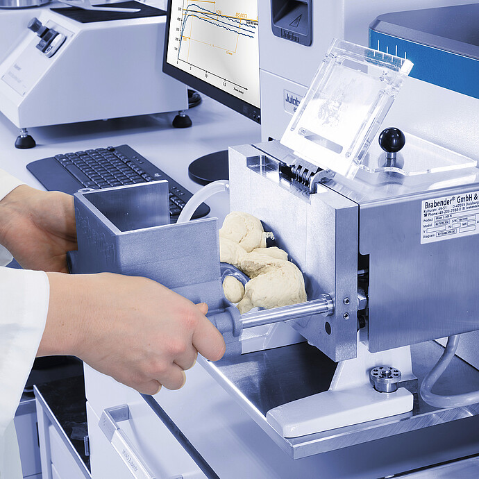 Close-up of technician loading dough into Brabender FarinoGraph mixing chamber, with open lid and visible kneading blades in laboratory setup