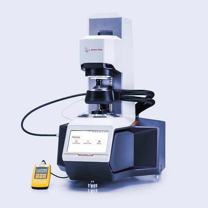 Anton Paar SmartPave 303 rheometer with connected temperature-control hoses and a handheld digital meter on a light background.