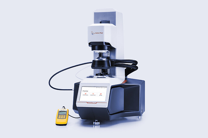 Anton Paar SmartPave 303 rheometer with connected temperature-control hoses and a handheld digital meter on a light background.