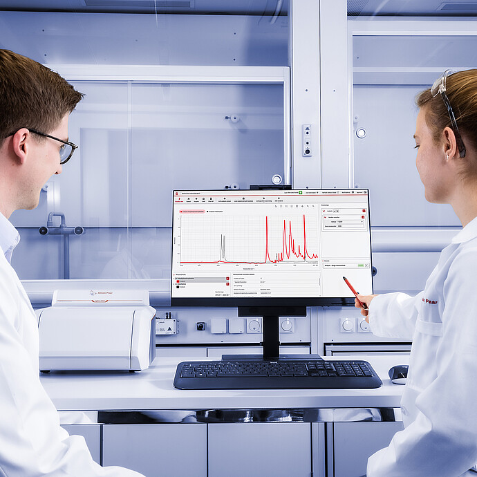 Two laboratory technicians working with an Lyza 3000 FTIR spectrometer placed on the bench in front of a central monitor displaying the Spectroscopy Suite spectral analysis software