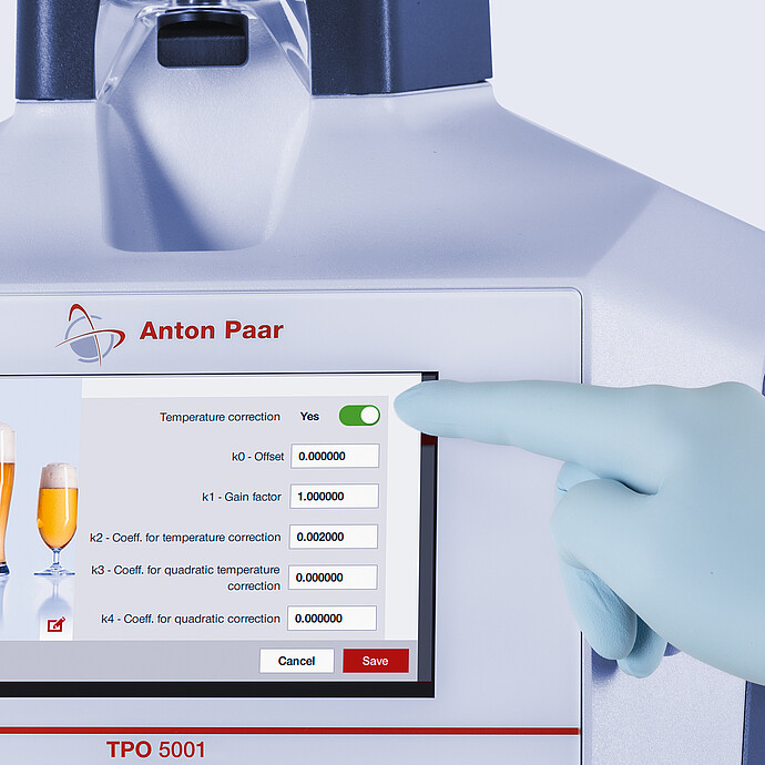 Gloved hand adjusting temperature correction settings on the touchscreen of the Anton Paar TPO 5001 Total Package Oxygen Meter.