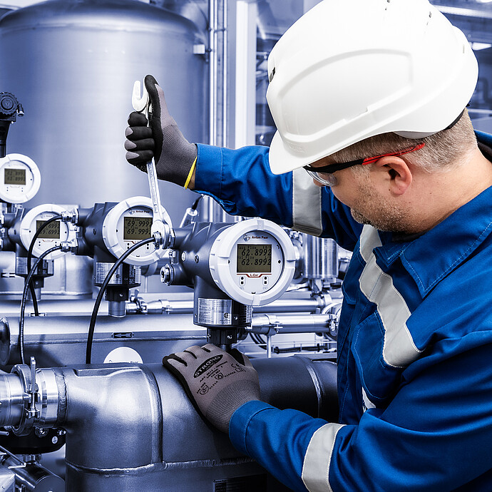 Technician in safety gear using a wrench to adjust an installed Anton Paar L-Cor 8000 Coriolis flow meter on stainless steel piping system.