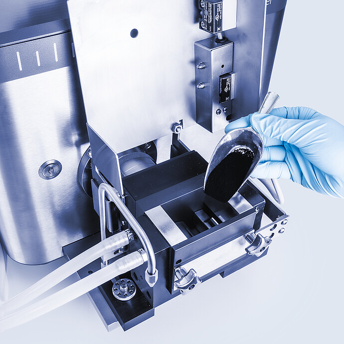 Close-up of Brabender AbsorptoMeter measuring chamber as gloved technician adds powder sample with scoop, sigma blades and tubing visible