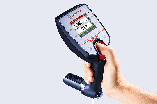 Hand holding Anton Paar DMA 35 portable density meter showing density and temperature measurement on integrated display.