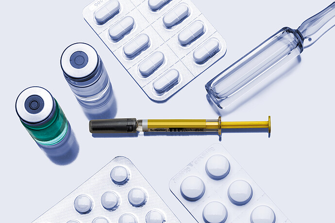 Pharmaceutical items including vials, glass ampoule, prefilled syringe, and blister packs with tablets arranged on a neutral background