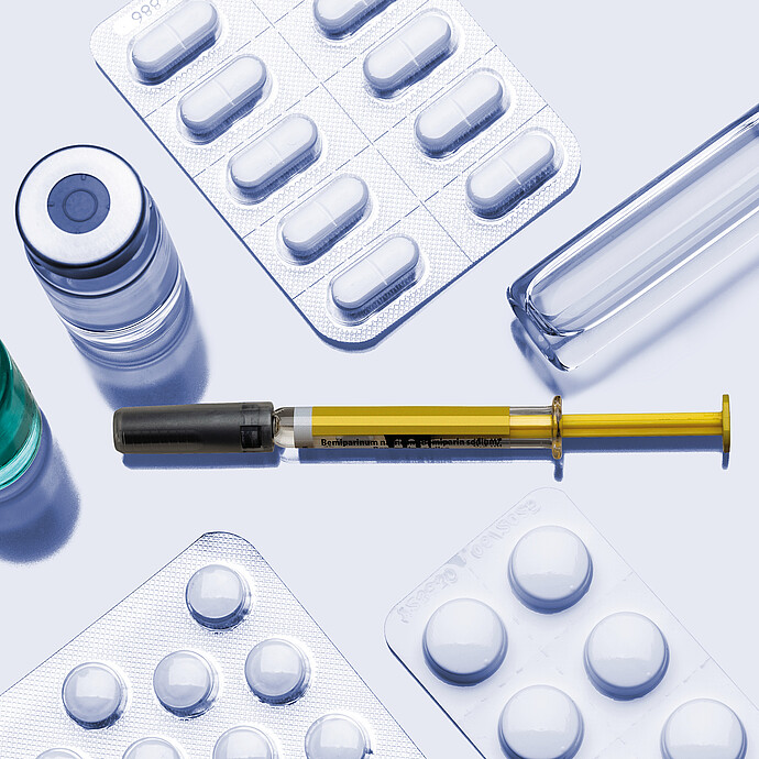 Pharmaceutical items including vials, glass ampoule, prefilled syringe, and blister packs with tablets arranged on a neutral background