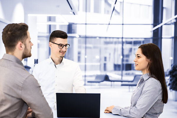 Three Anton Paar colleagues having a discussion at a laptop in a bright office with glass walls and modern furnishings.