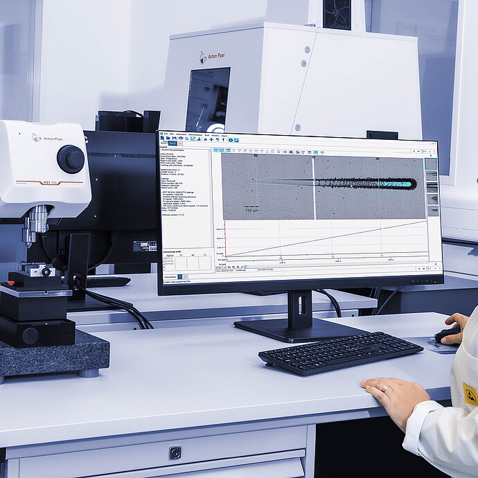 A technician operating the Anton Paar Revetest® Scratch Tester RST 100 in a laboratory, reviewing scratch test data displayed on a computer monitor.