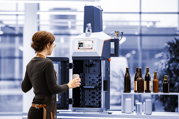 Technician loading a beverage can into the Anton Paar TPO 5001 Total Package Oxygen Meter; various bottles and cans shown for compatibility.