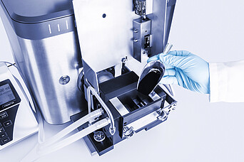 Brabender AbsorptoMeter with mixer as a gloved technician adds carbon black powder using a metal scoop into the mixing chamber