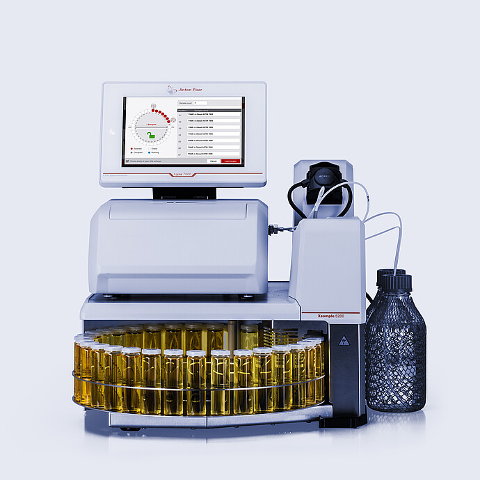 Anton Paar Lyza 7000 FTIR spectrometer with Xsample 5200 autosampler, sample carousel with yellow liquid vials, tubing, and bottle.