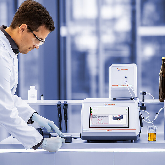 Lab technician using Anton Paar Enzymatic Reader with DMA 5002, Alcolyzer 3001, and Xsample 3100 beside beer bottles and sample beaker.