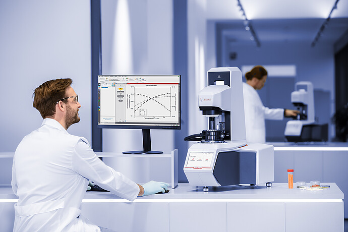 Lab technician reviews results beside an Anton Paar SmartMelt 73 polymer melt rheometer in a laboratory.