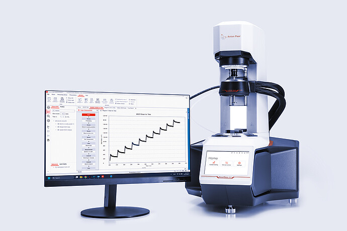 Anton Paar SmartPave 303 rheometer beside a monitor showing RheoCompass test data and a strain-time graph.