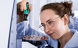 Technician assembling or repairing an electronic circuit board inside a laboratory device using a screwdriver.