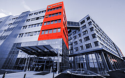 Anton Paar headquarters in Graz, Austria, showcasing a modern building with a distinctive red and gray facade, glass entryway, and connecting architectural bridge