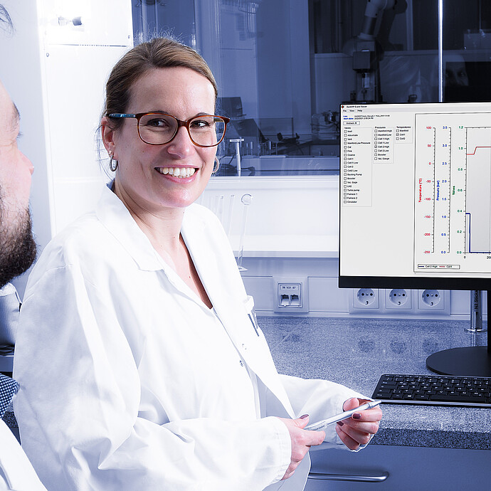 Two laboratory technicians in lab coats reviewing data on a monitor displaying graphical logs of pressure and temperature readings from the Anton Paar iSorb HP gas sorption analyzer. The system interface includes animated diagnostics and valve operation logs for maintenance planning and analysis playback.