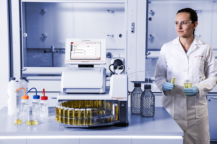 Laboratory technician holding sample tubes beside Anton Paar Lyza 7000 FTIR spectrometer with Xsample 5200 autosampler.