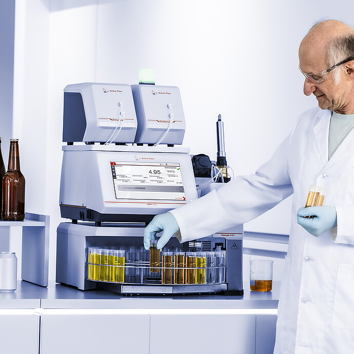 Technician handling beer samples beside Anton Paar RTD Measurement System with DMA 5002, HazeQC ME, Alcolyzer ME, and Xsample 5100.