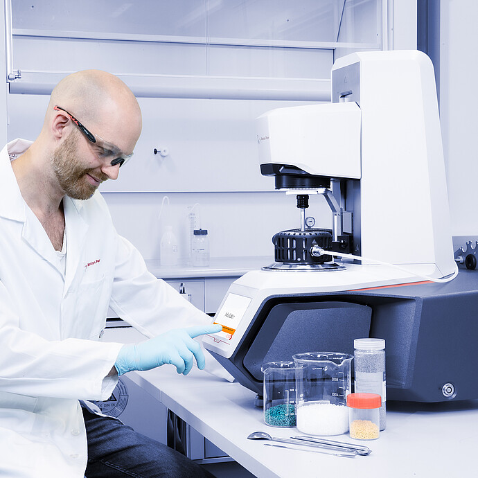 Technician in safety glasses operating an Anton Paar Modular Compact Rheometer MCR with sample beakers on a lab bench