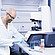 Technician in safety glasses operating an Anton Paar Modular Compact Rheometer MCR with sample beakers on a lab bench