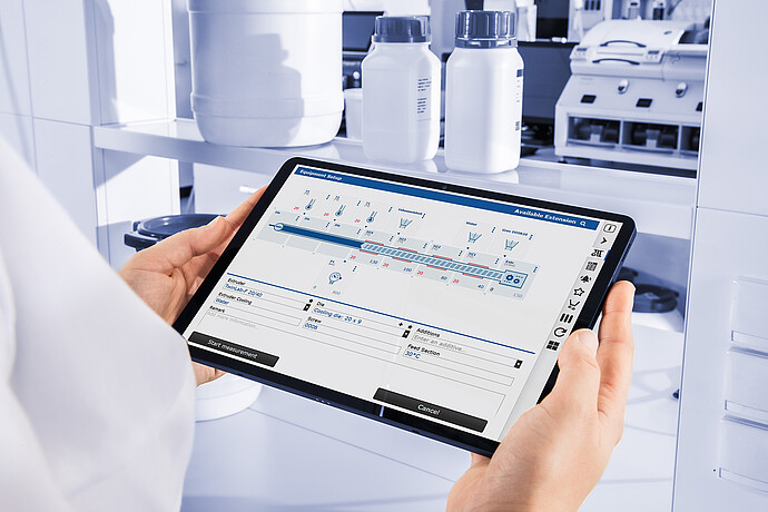 Technician holding tablet displaying Brabender TwinLab B-TSE-S-30-40 control interface, with laboratory containers and equipment in background